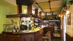 A bar area with wooden counters, stools, and shelves stocked with bottles and glasses. - Armanac De Toubie (Arnad)
