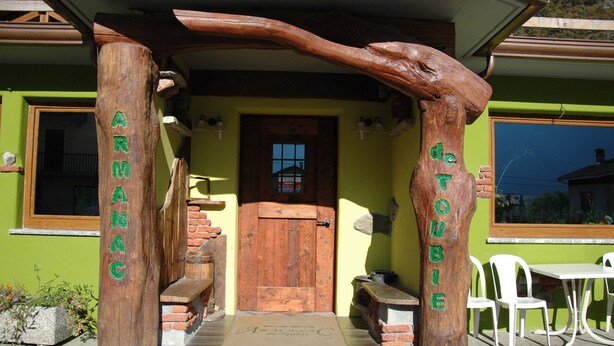 A wooden archway with the words "ARMANAC" and "de TOUBIE" carved into it, leading to a door with a window above. - Armanac De Toubie (Arnad)