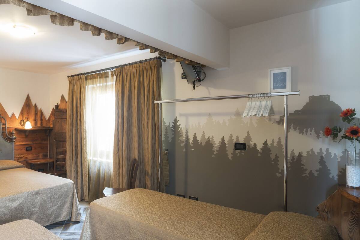 Habitación con dos camas, decoración de pared de madera con motivos de montaña, un espejo y una ventana con cortinas.