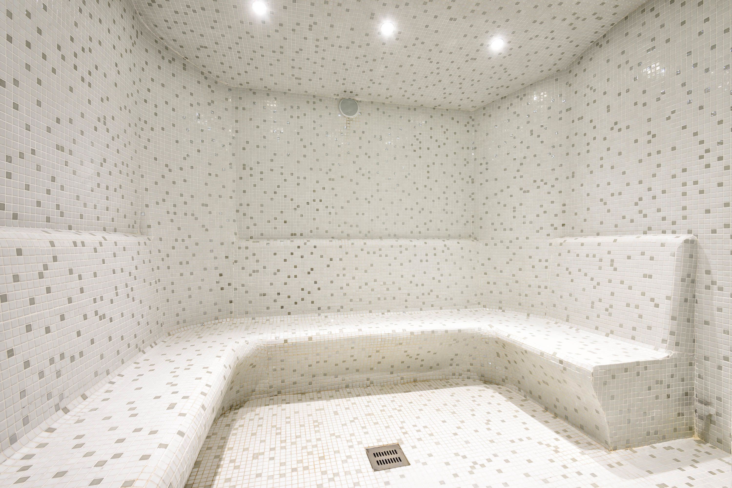 A small, tiled room with a bench and a drain in the center.