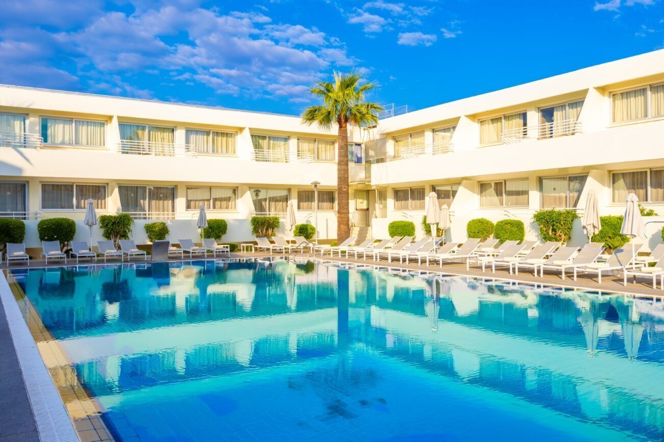 A hotel with a swimming pool surrounded by sun loungers and palm trees.
