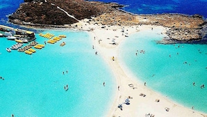 Luchtbeeld van een strand met helder turquoise water, een zandstrand en verschillende gele boten afgemeerd bij de kust.