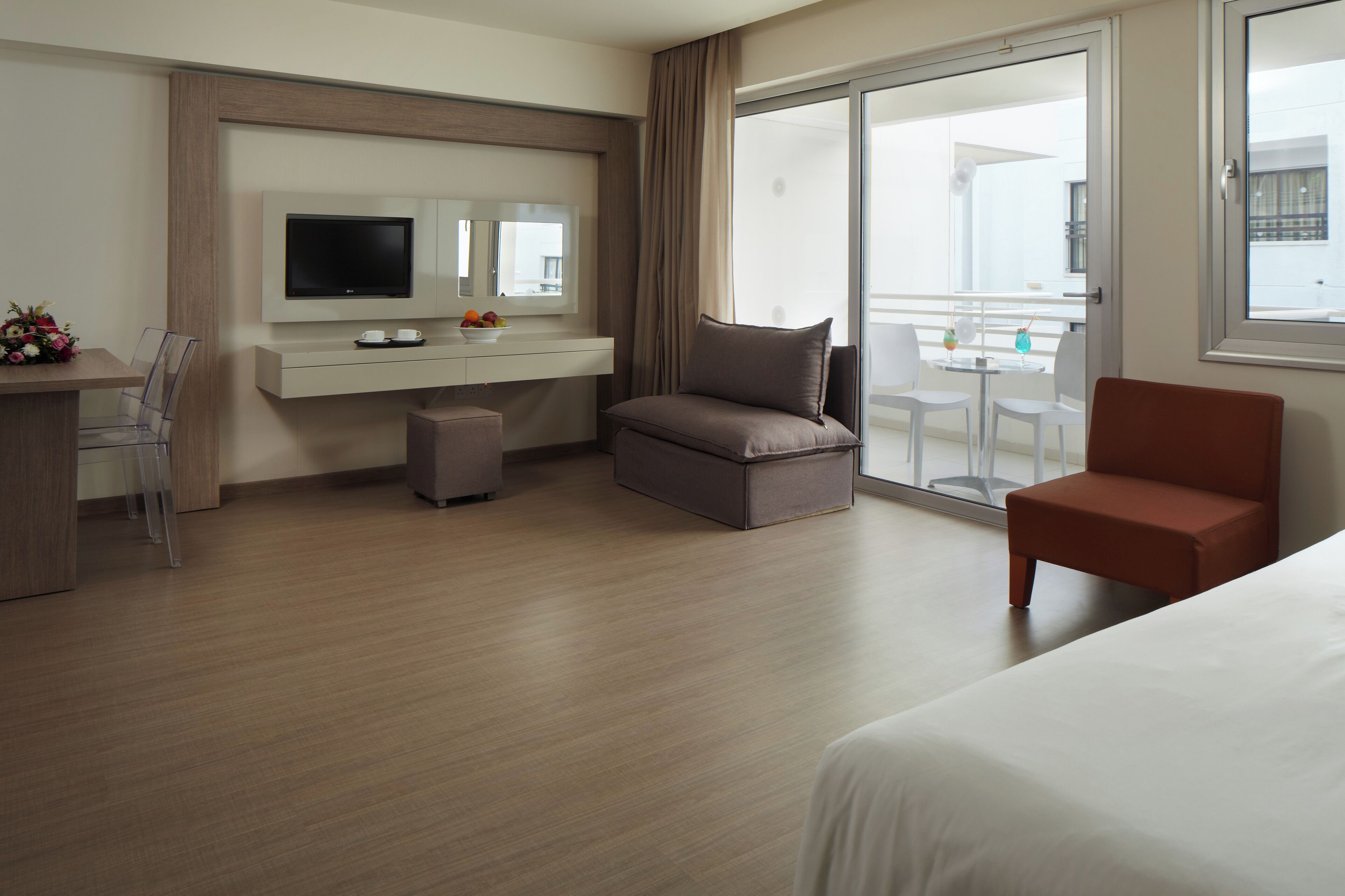 A hotel room with a bed, a TV, a desk, and a balcony with a table and chairs.