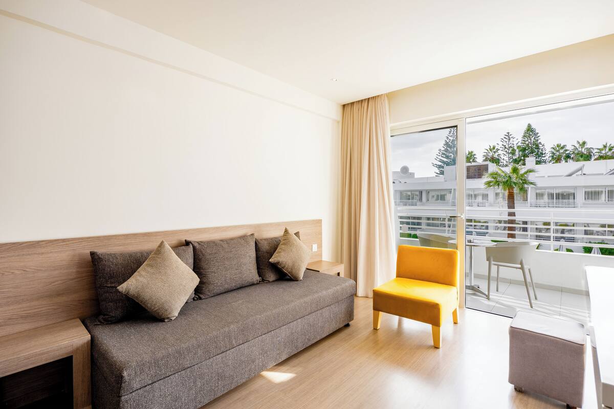 Een moderne hotelkamer met een grijze bank, een gele fauteuil en een eettafel.
