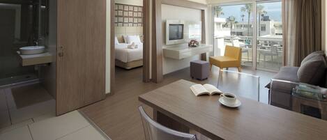 A modern hotel room with a balcony, a dining area, and a bedroom with a TV and a bed.