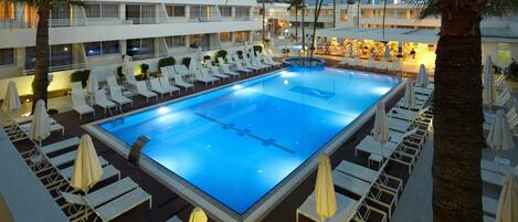 Una amplia piscina interior con varias zonas de descanso y palmeras.