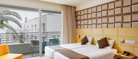 Ein Hotelzimmer mit einem großen Bett, einem kleinen Nachttisch mit Telefon, einem Sessel und einem Balkon mit Blick auf die Stadt.