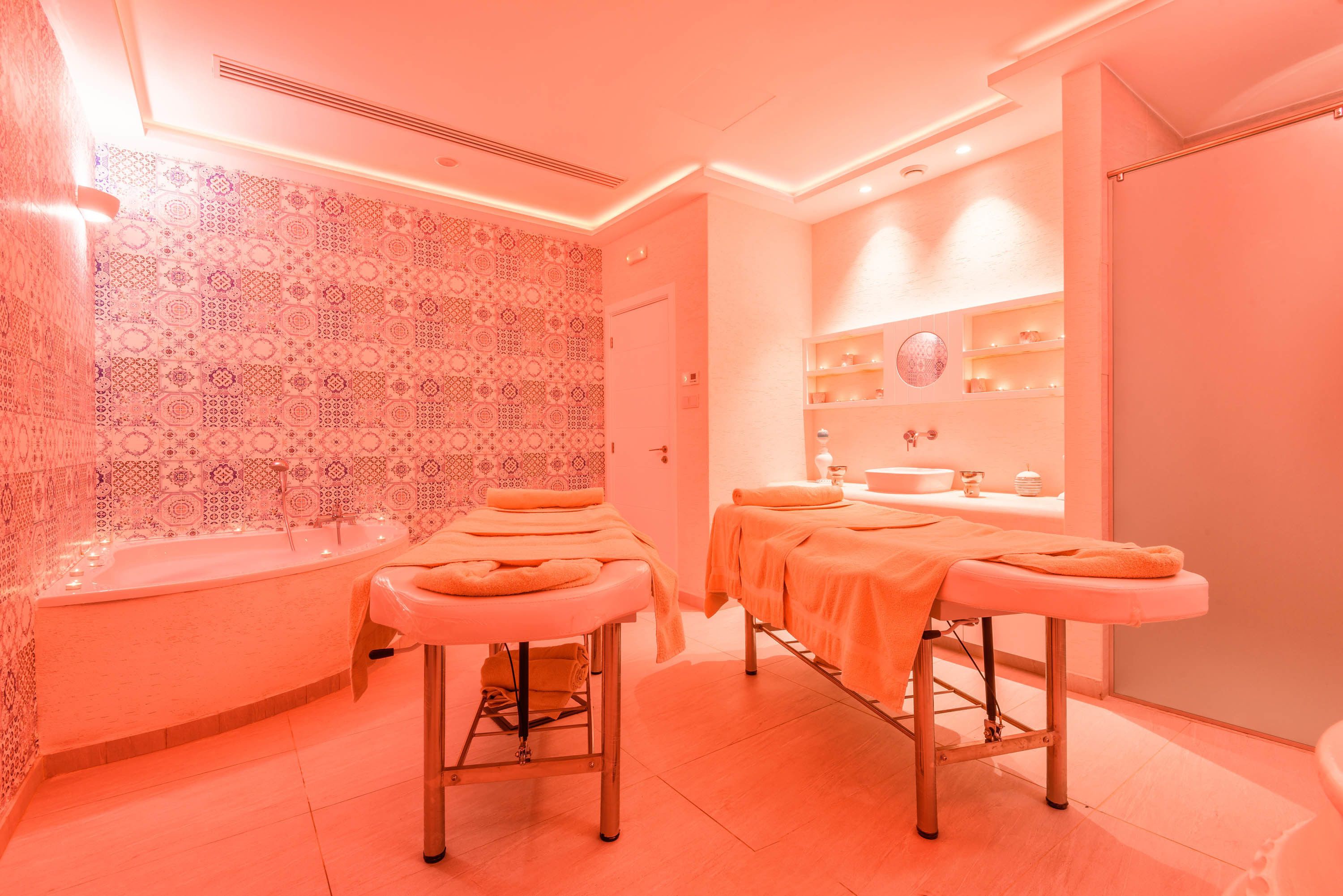 A spa room with two treatment tables, a bathtub, and a shelf with toiletries.