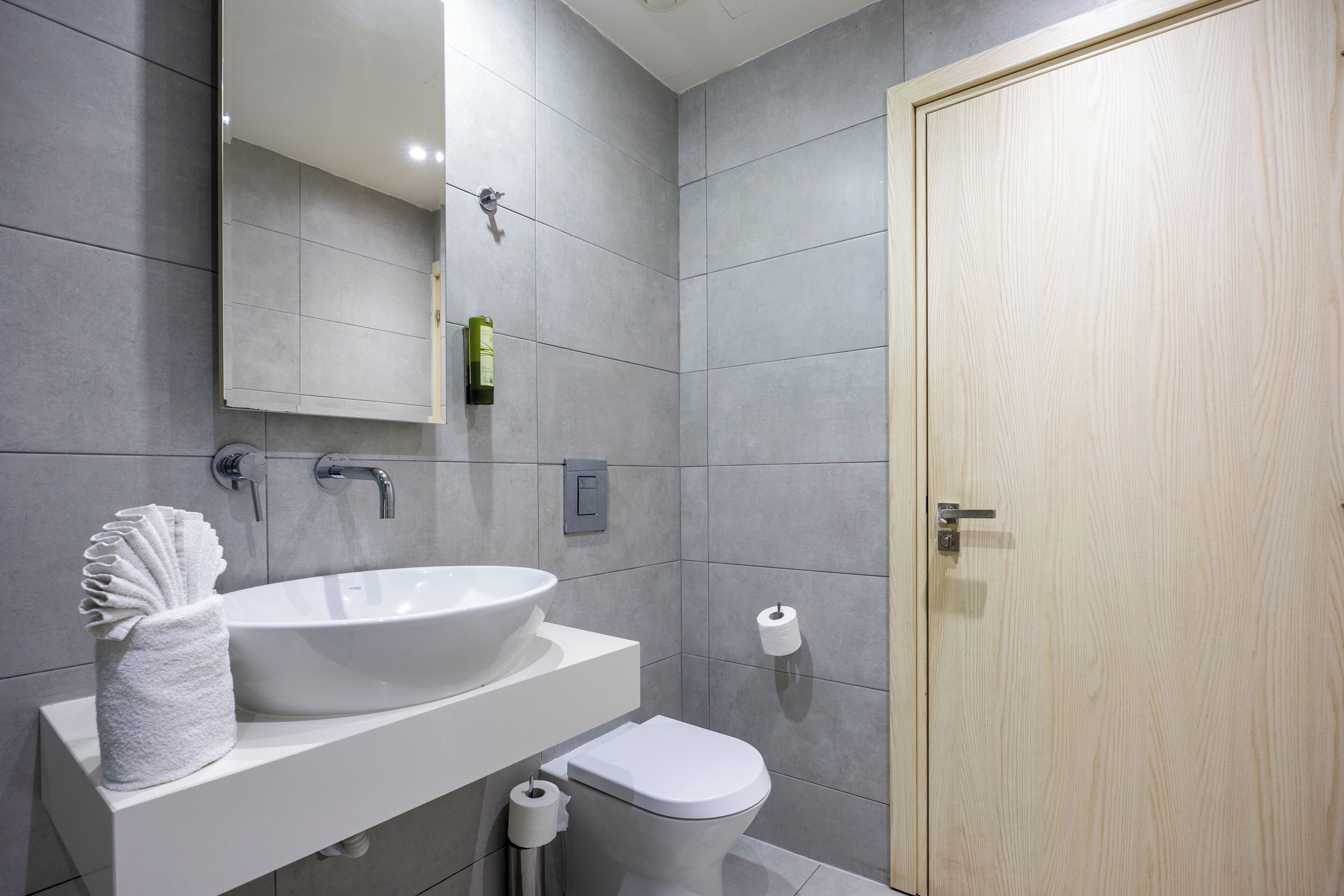 A modern bathroom with a white sink, a toilet, and a wooden door.