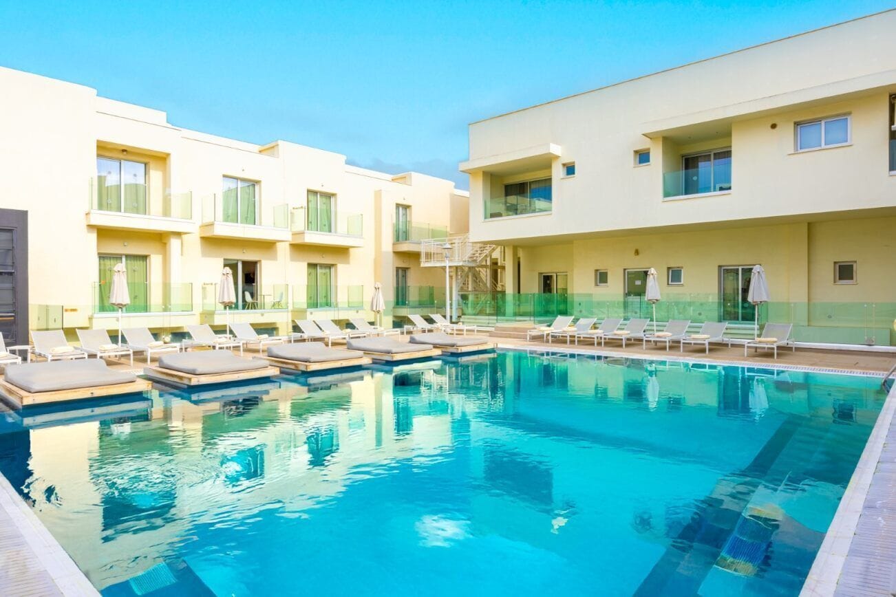 A swimming pool with lounge chairs and a building with balconies.