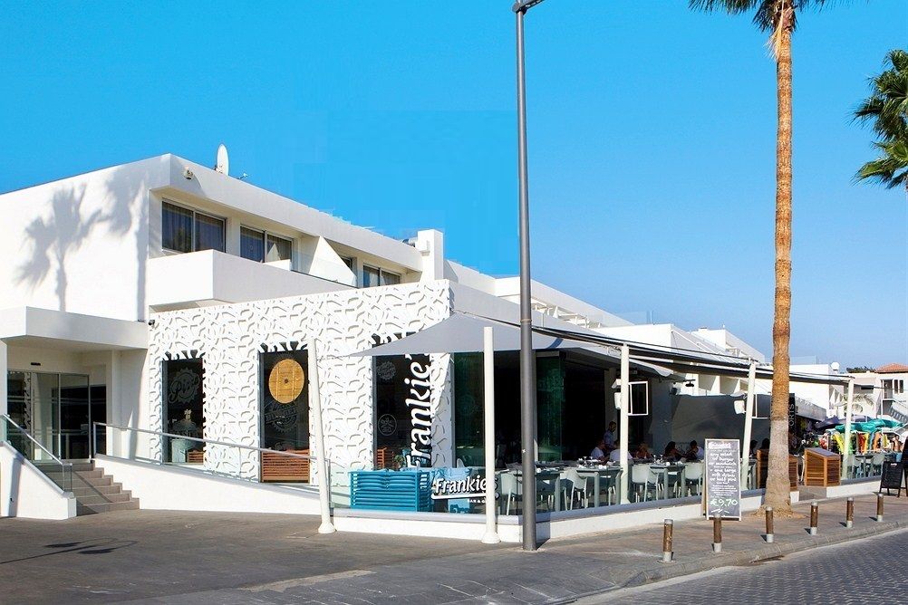 A modern building with a white facade, a covered outdoor seating area, and a sign reading "Frankie."