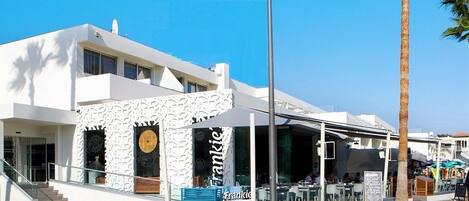 A modern building with a white facade, a covered outdoor seating area, and a sign reading "Frankie."