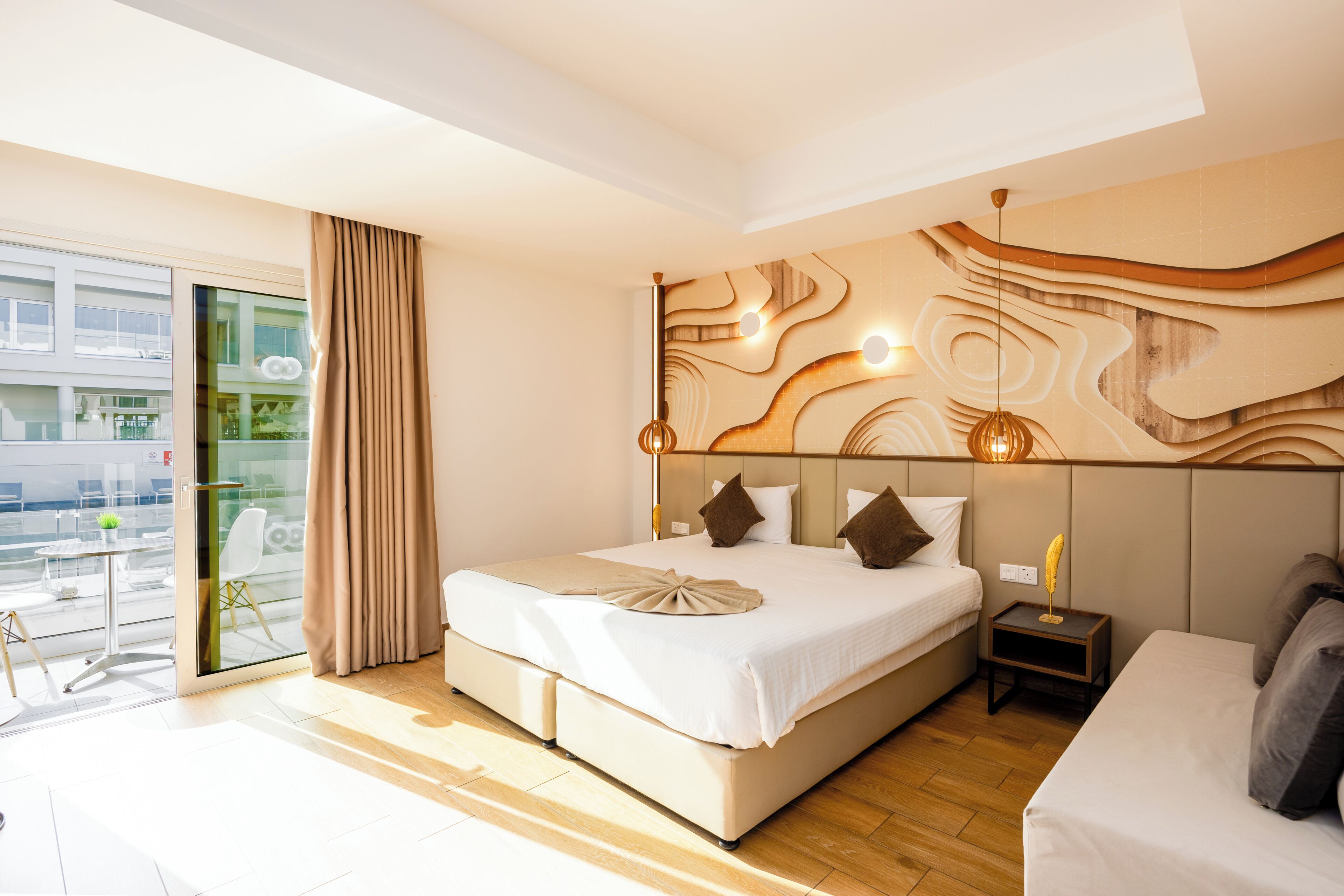 Ein modernes Hotelzimmer mit einem großen Bett, einem Nachttisch, einer Fenstersturz und Blick auf die Stadt durch eine Glastür.