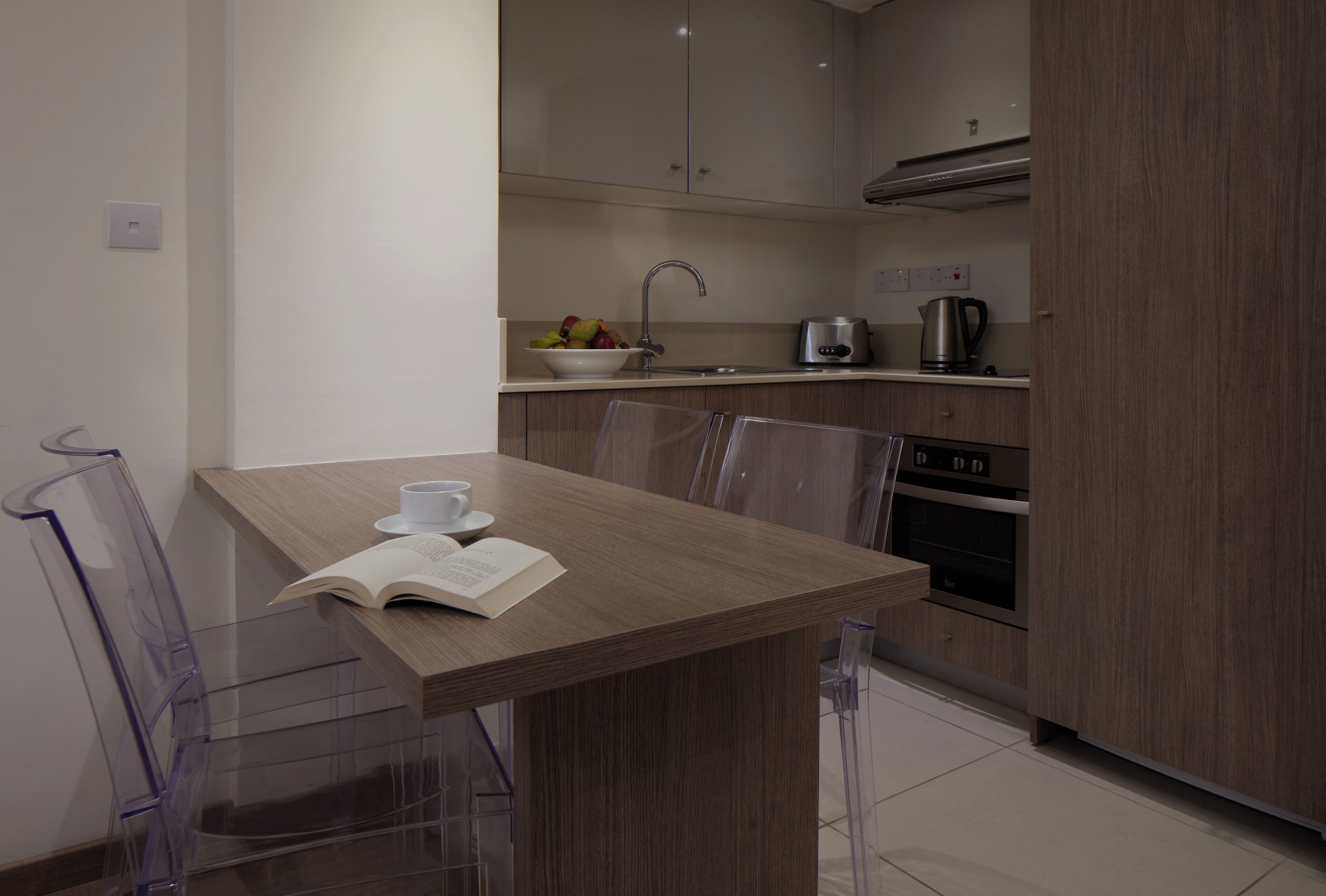 Une cuisine moderne avec un coin repas, comprenant une table avec des chaises, une bouilloire et un saladier de fruits.