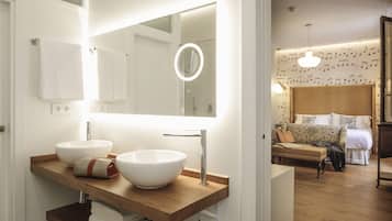 A modern bathroom with two large white sinks, a wooden vanity, a mirror with a light, and a visible shower area.