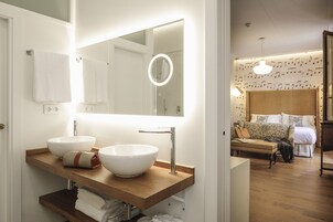 Un baño moderno con dos lavamanos grandes blancos, un mueble de tocador de madera, un espejo con luz y una zona de ducha visible.