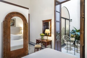 Une chambre d’hôtel avec un grand miroir décoratif, un lit, un bureau avec une lampe et une petite table avec des chaises.