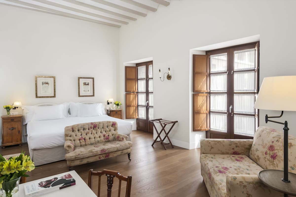 Une chambre à coucher avec un lit, deux tableaux encadrés, une table de chevet, un canapé à motifs floraux, une petite table et une lampe.