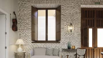 Une pièce avec un mur en pierre, un plafond en bois, une grande fenêtre, un canapé, un fauteuil, une lampe et un violon.