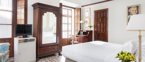 A hotel room with a bed, a TV, a desk, a wardrobe, and a patterned floor.
