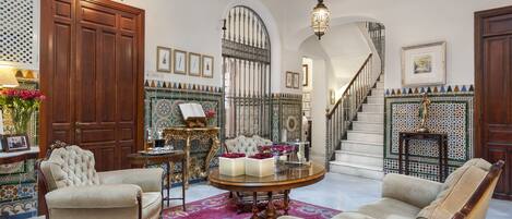 Una sala de estar lujosa con una imponente escalera, muebles ornamentados y azulejos decorativos.
