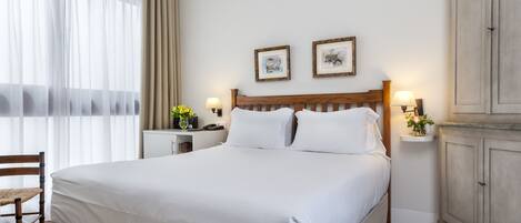 A neatly made bed with white linens, a wooden headboard, and two bedside tables with lamps.