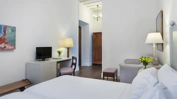 Une chambre d’hôtel avec un lit, un bureau avec une télévision, une chaise, une petite table, une lampe et un tableau au mur.