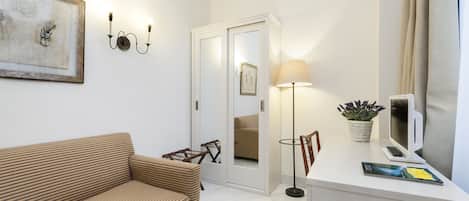 A modern hotel room with a sofa, a desk with a computer, a lamp, and a mirror.