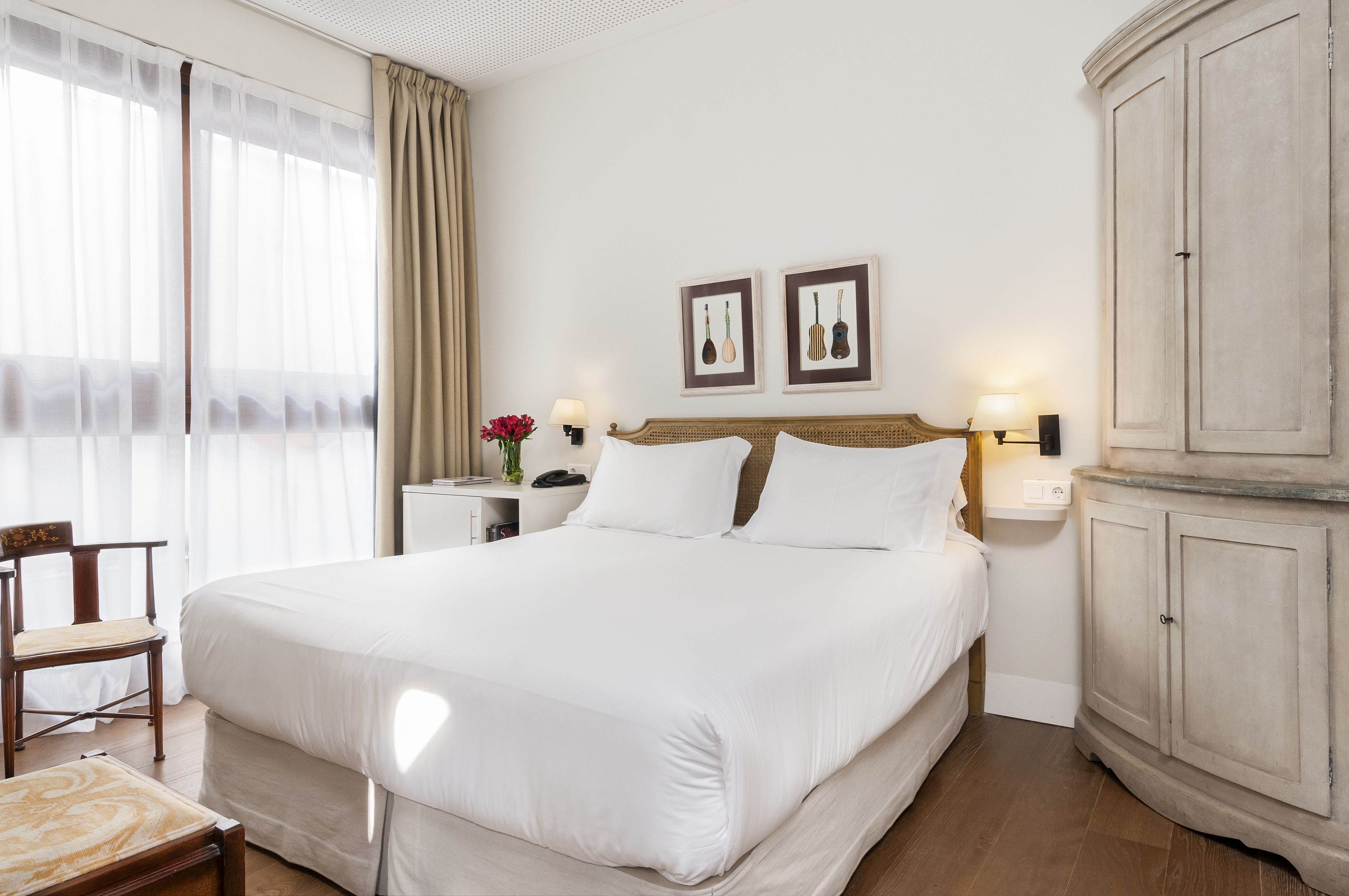 Una habitación de hotel ordenada con una cama grande, una silla de madera, una mesita de noche con lámpara y un armario.