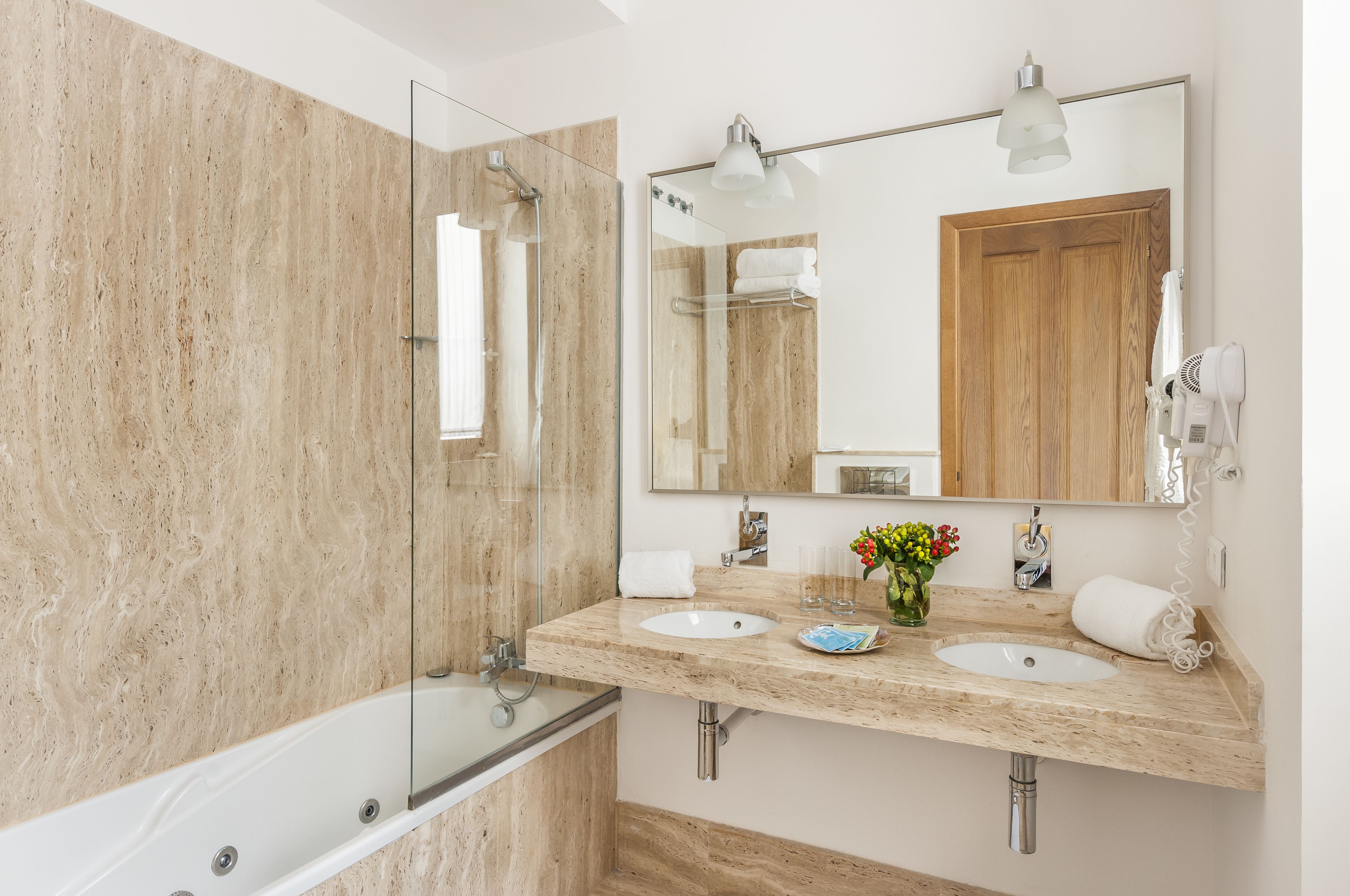Een moderne badkamer met een douchecabine van glas, twee wastafels, een grote spiegel en een houten deur.