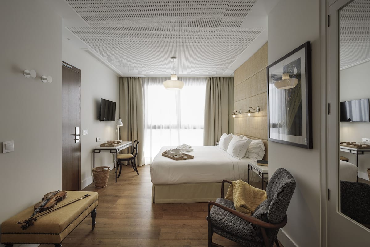 Une chambre d’hôtel avec un grand lit, un bureau, une chaise, un violon et un téléviseur.
