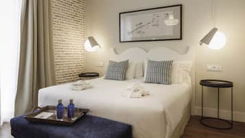 A neatly arranged bedroom with a large bed, two bedside tables, a hanging light fixture, a framed artwork, and a wooden floor.