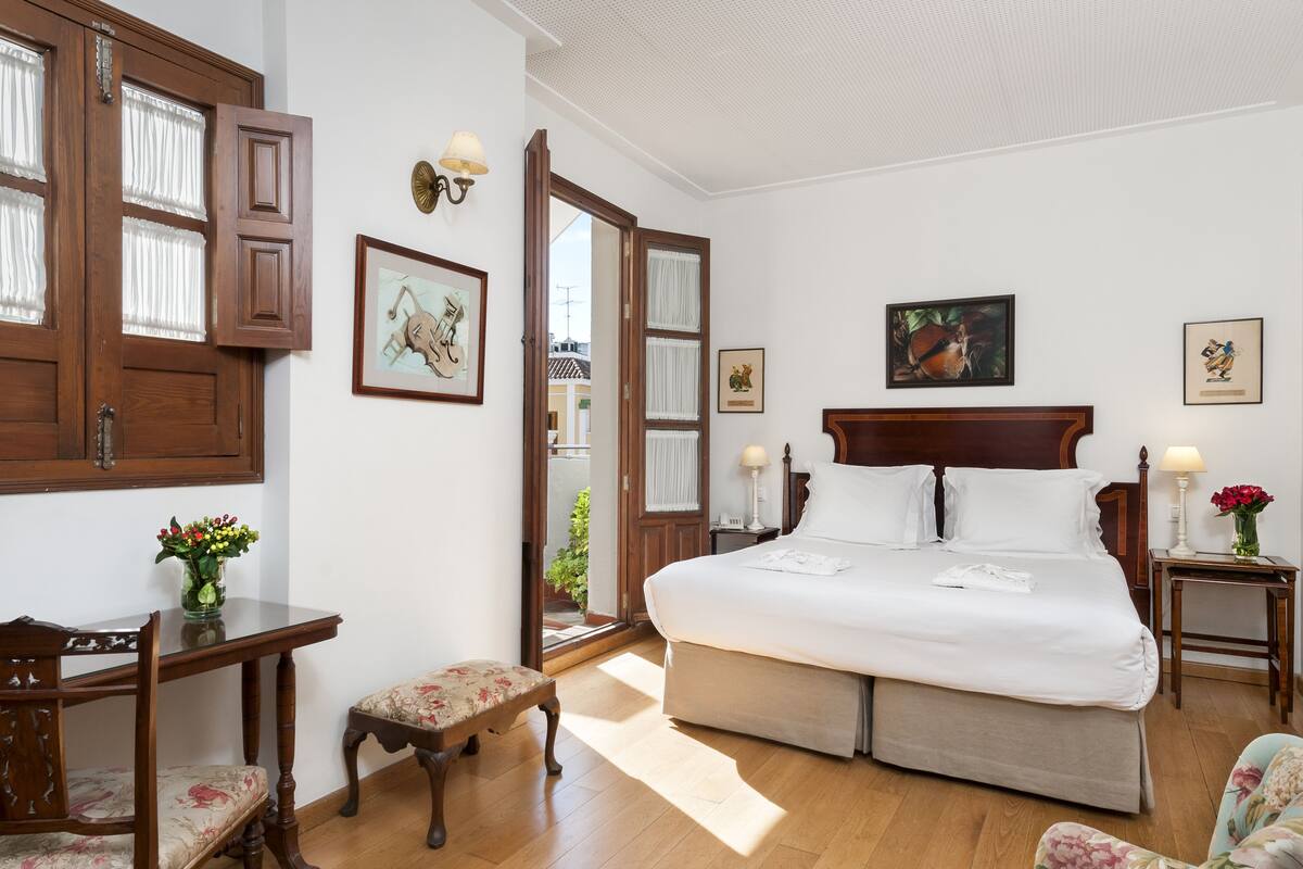 Une chambre spacieuse avec un grand lit, des meubles en bois et des œuvres d’art encadrées accrochées aux murs.