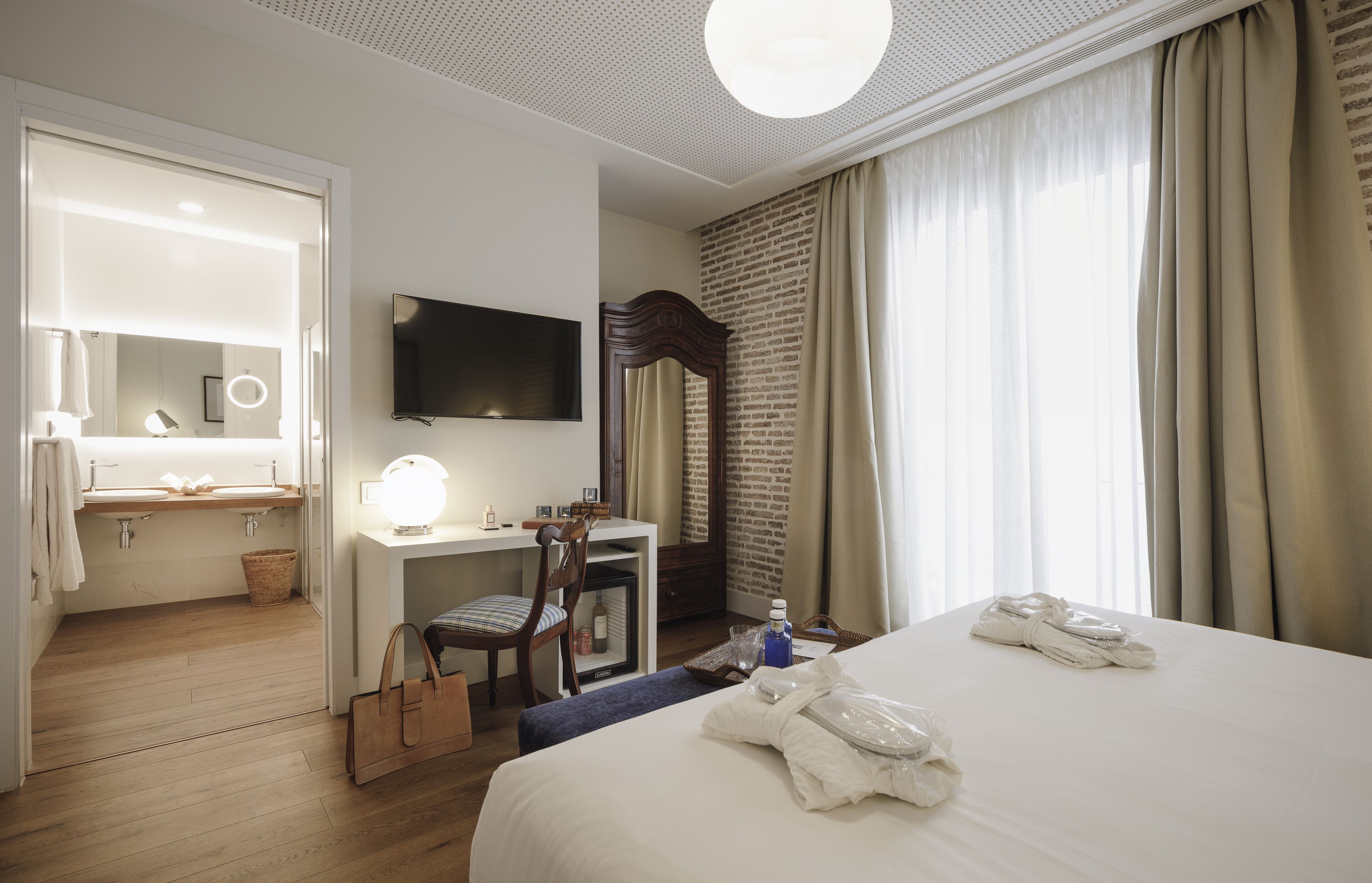 Een hotelkamer met een bed, een bureau met stoel, een televisie, een spiegel en een badkamer met wastafel en handdoekhouder.