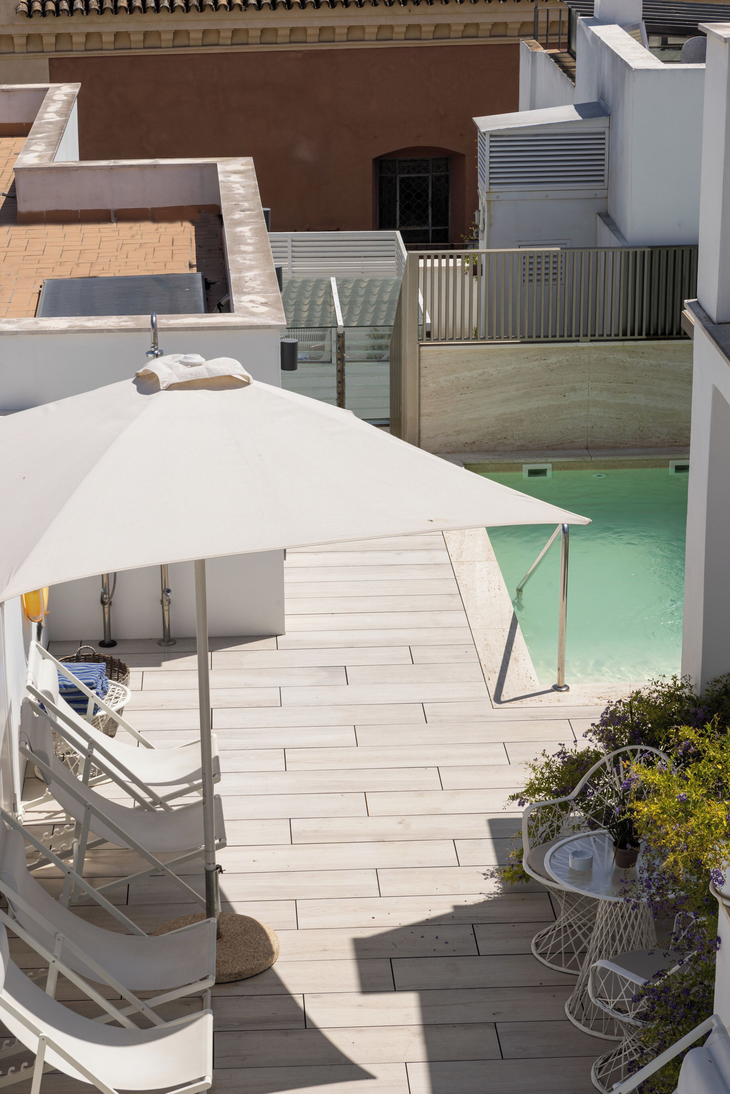 A rooftop terrace with a swimming pool, white outdoor furniture, and a white umbrella providing shade.