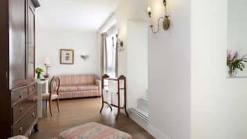 A room with a wooden dresser, a floral sofa, a wooden chair, a small table with a lamp, and a wall-mounted light fixture.