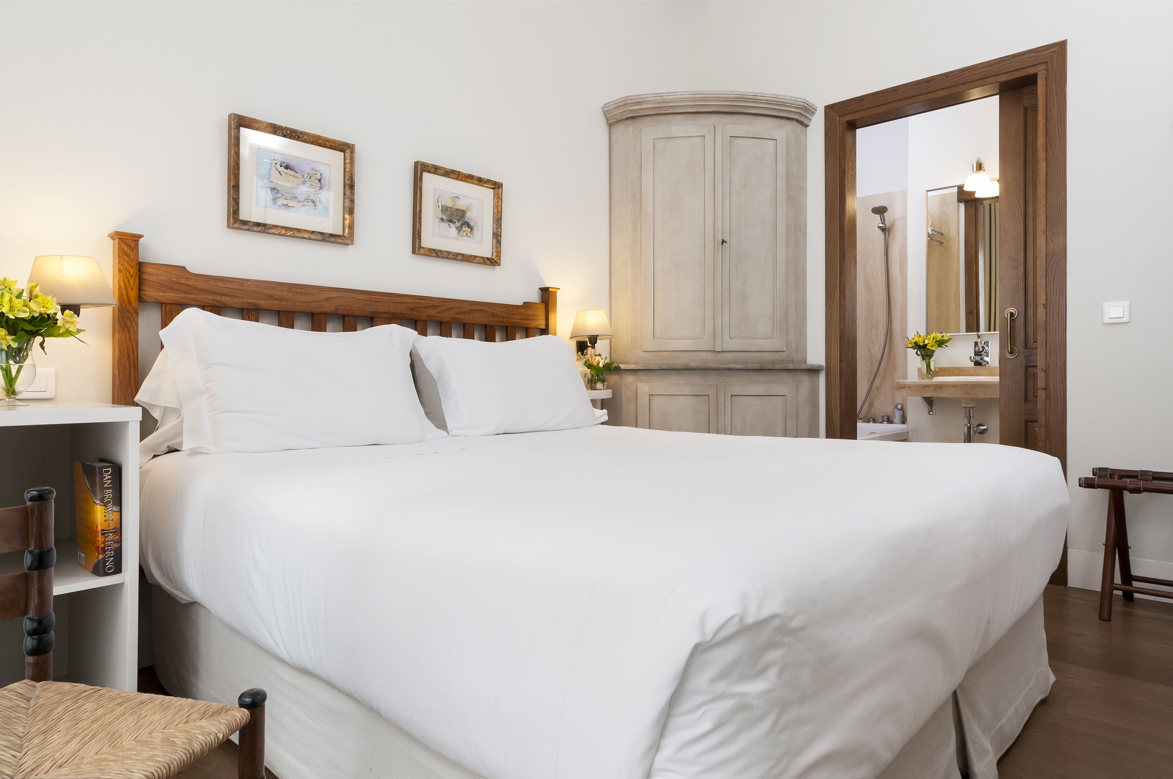 Een net opgemaakt bed met witte lakens, een houten hoofdbord en twee ingelijste foto’s aan de muur.