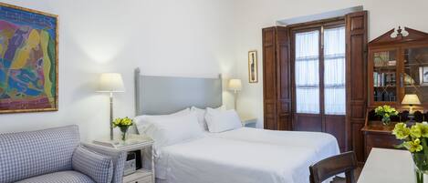 Una habitación de hotel con cama, sofá, escritorio, lámpara y ventana con cortinas.