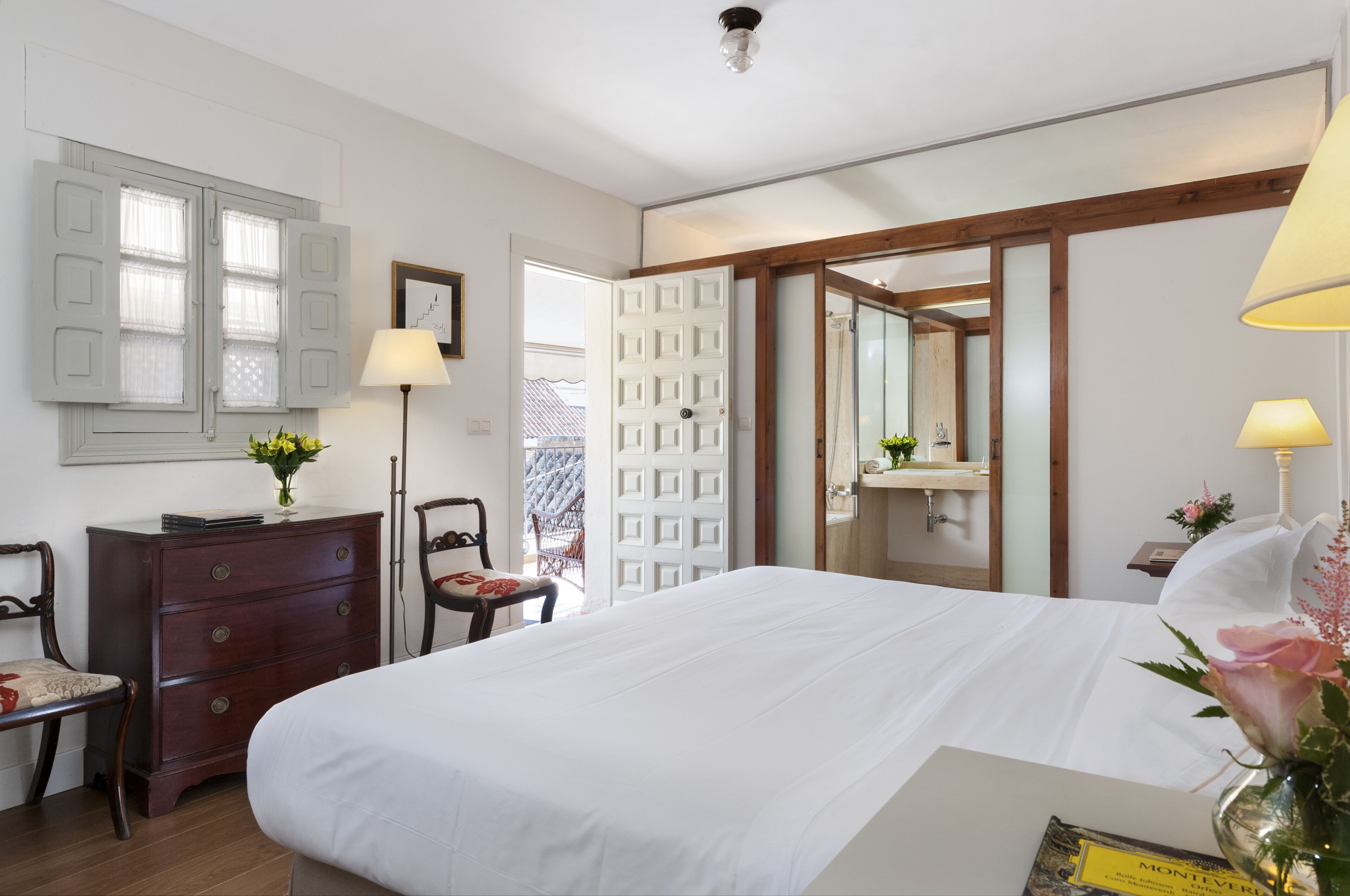 Habitación de hotel con una cama grande, cómoda, escritorio, lámpara, espejo y puerta que da a un balcón.