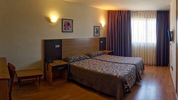A hotel room with two beds, a desk, a chair, and a TV.