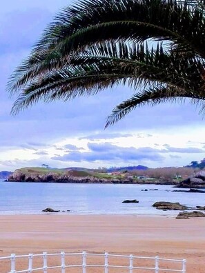 A beach with a white fence, calm water, and a distant view of hills and a small building. - Hotel Piedra (Carreno)