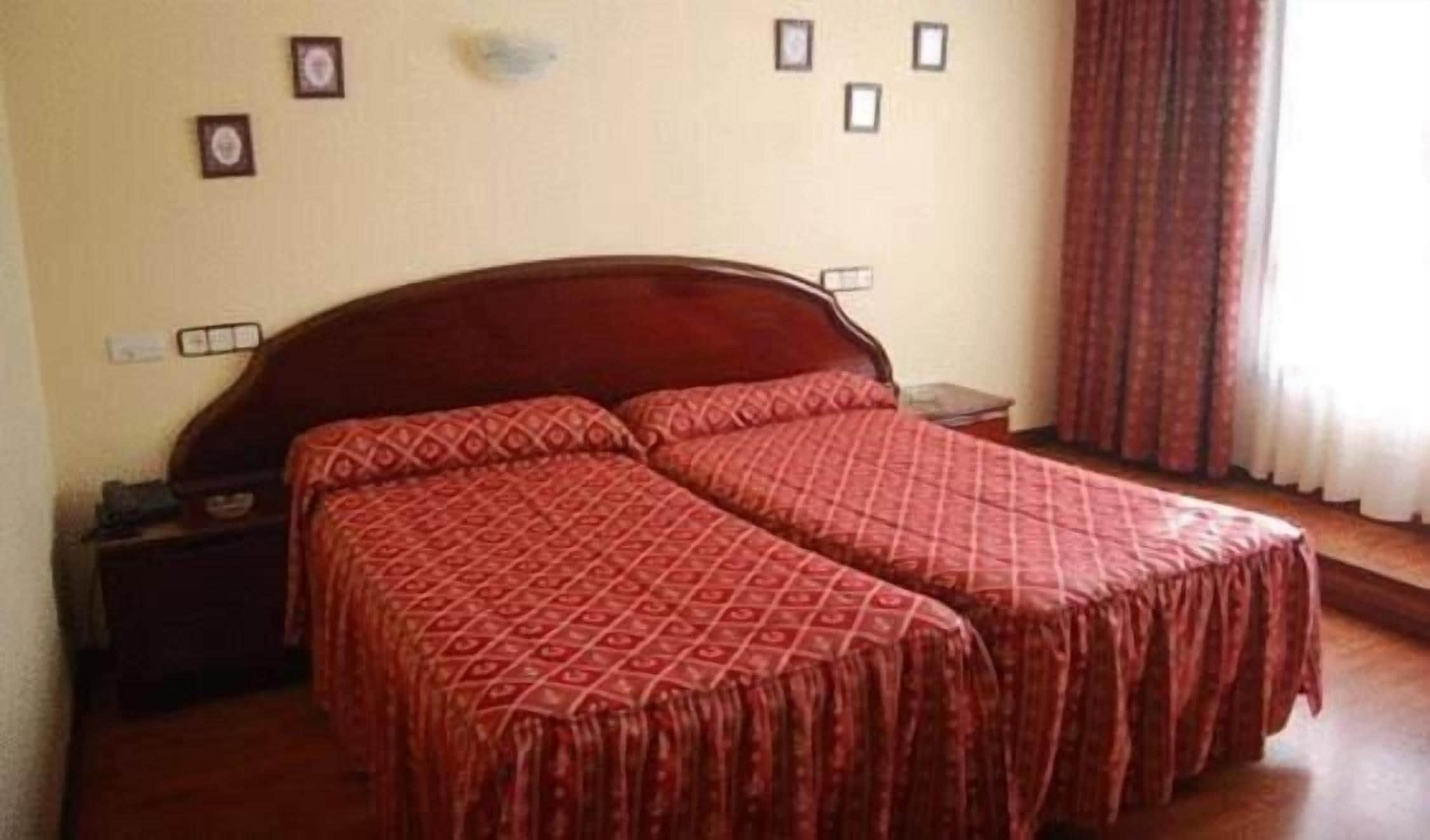 Cama doble con una colcha roja estampada en una habitación de hotel.