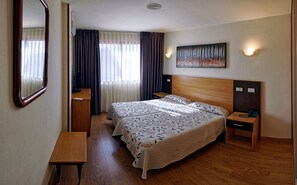 A hotel room with a wooden bed, a desk, a mirror, a painting, and a nightstand with a phone. - Hotel Piedra (Carreno)