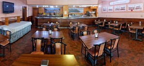 A restaurant with multiple tables and chairs, a bar area with a counter and various bottles, and a television mounted on the wall. - Hotel Piedra (Carreno)