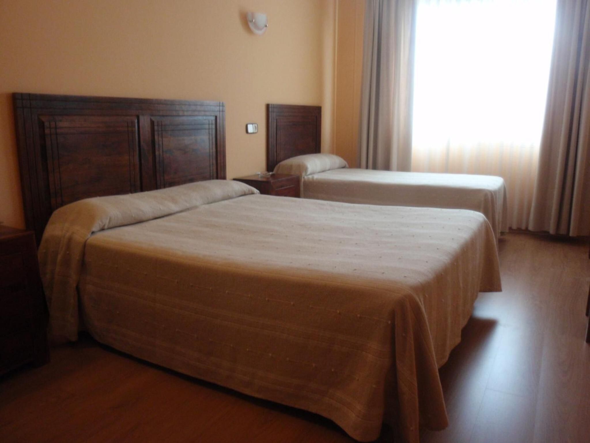 Une chambre d’hôtel avec deux lits simples, des têtes de lit en bois, une table de chevet et une fenêtre avec des rideaux.
