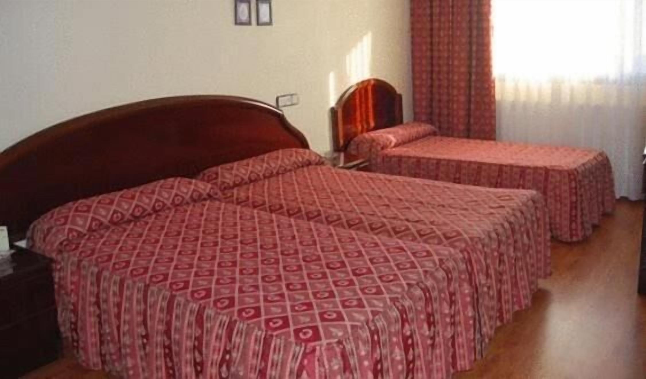 A room with a large bed and two smaller beds with matching patterned bedding.