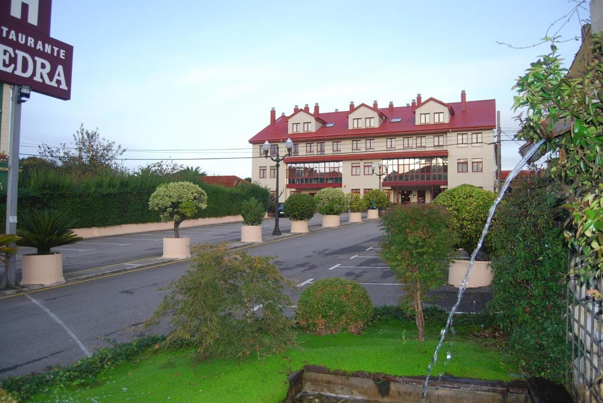 A hotel with a red roof and multiple windows, surrounded by well-maintained greenery and a parking area.