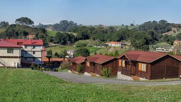 Entorno rural con una mezcla de cabañas modernas y de madera tradicional, una carretera pavimentada y un paisaje montañoso con árboles y cielo despejado.