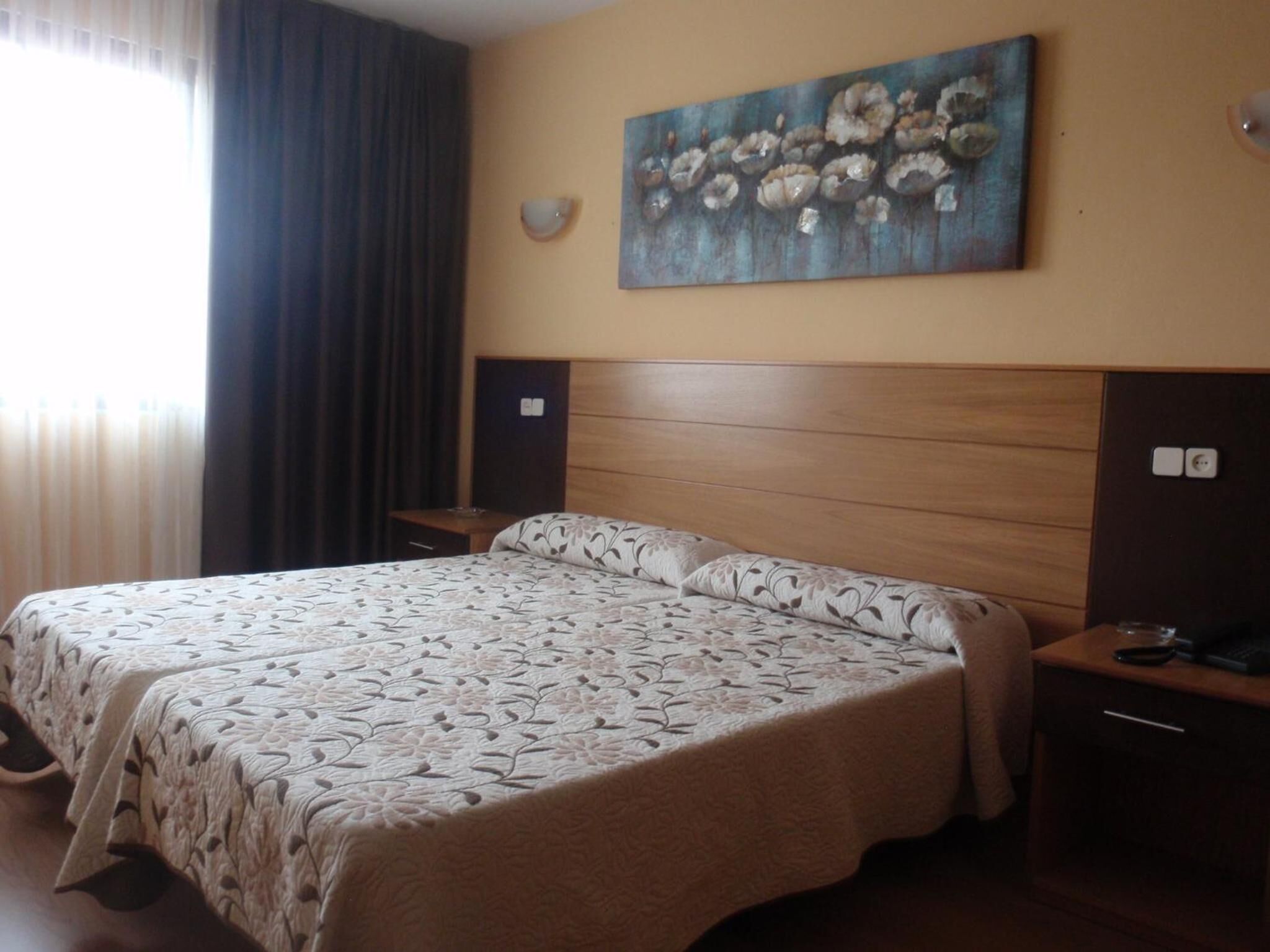 Une chambre d’hôtel avec un grand lit, une tête de lit, une table de chevet, une lampe fixée au mur et un tableau.