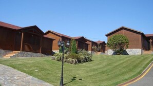 A row of wooden cabins with stone steps leading up to the entrance, surrounded by well-maintained grass and a few trees. - Hotel Piedra (Carreno)